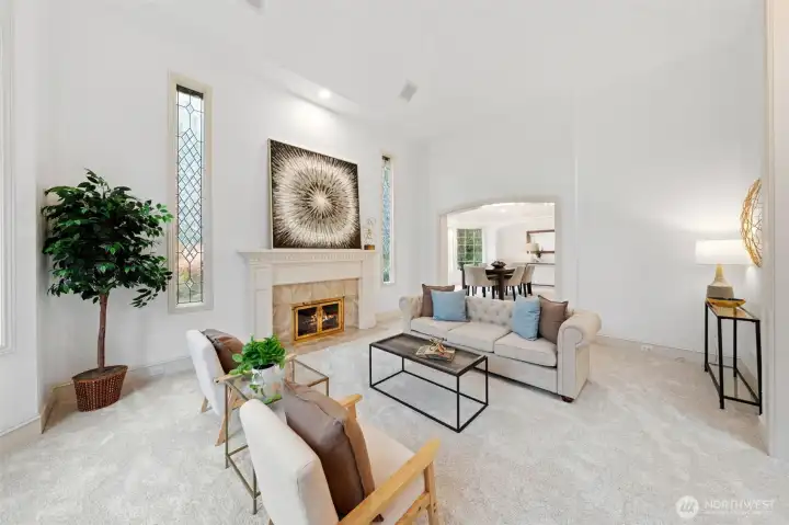 Soaring ceilings, dramatic fireplace, and tall leaded-glass windows create a bright, elegant living space with a sense of volume and refined architectural detail.