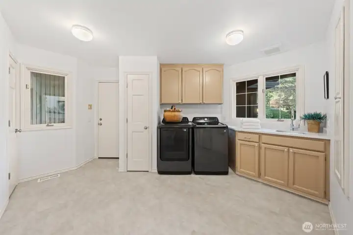 Spacious main-level utility room featuring washer and dryer, upon request, abundant cabinetry, and a convenient sink—designed for everyday functionality and easy household organization.The door to the left leads you to the three car-garage.