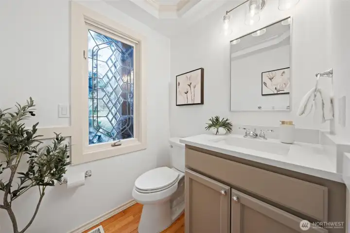Main-level powder room featuring an refinished vanity, quartz countertop, modern lighting, and a decorative leaded-glass window that adds natural light and character. Notice the craftsman throughout this home!