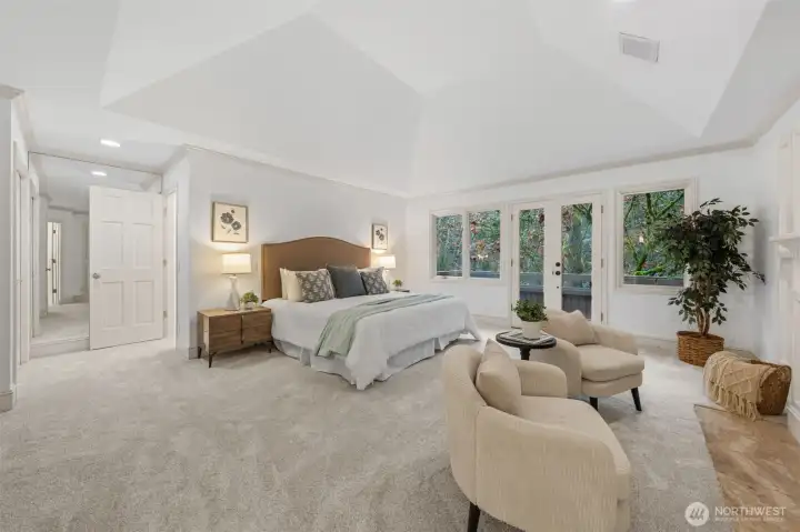 An expansive and serene Primary Suite showcasing soaring vaulted ceilings, plush new carpet, and fresh paint. Generous proportions easily accommodate a sitting area, while large windows and a private exterior door fill the room with natural light and tranquil, tree-lined views. To the back left is the walk-in closet.