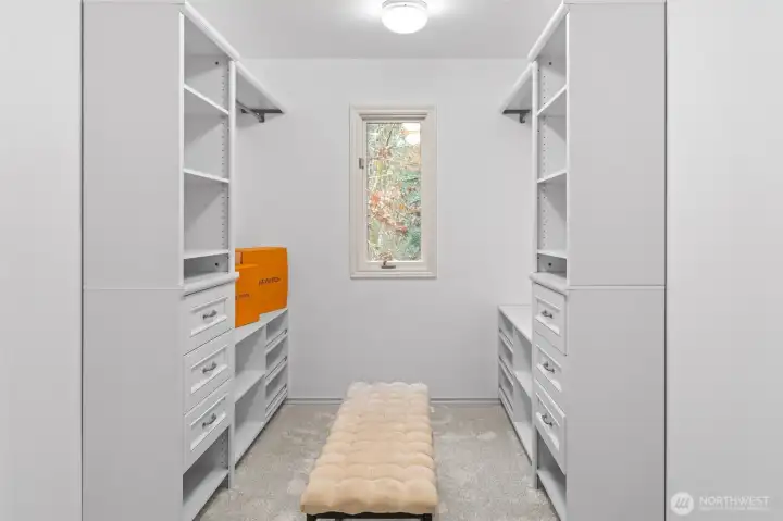 An organized and well-appointed primary walk-in closet with custom built-in shelving, drawers, and hanging space, plus a center bench and natural light—designed for both style and efficiency.