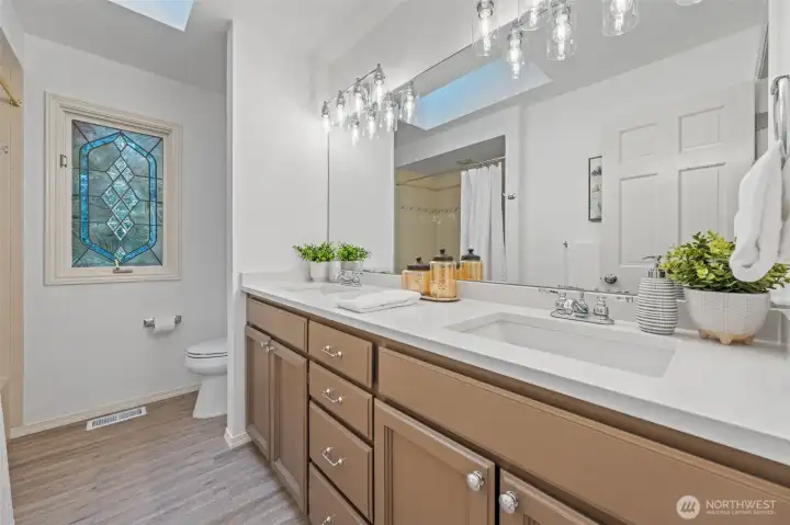 Main bathroom featuring a dual-sink vanity, modern lighting, and a skylight for natural light, complemented by fresh paint and updated fixtures. Notice the ceramic tile flooring for easy-care.