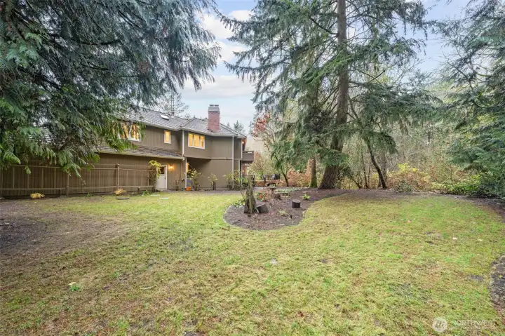 A wider perspective showcasing the home nestled into its private, wooded surroundings. The expansive lawn, towering trees, and natural buffer offer exceptional privacy, while the home and deck seamlessly connect indoor and outdoor living.