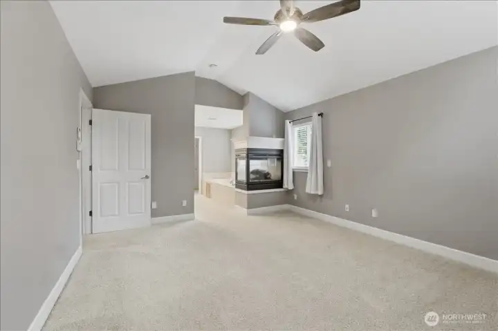 Opposite view of the primary bedroom with 3-sided gas fireplace leading into the bathroom.