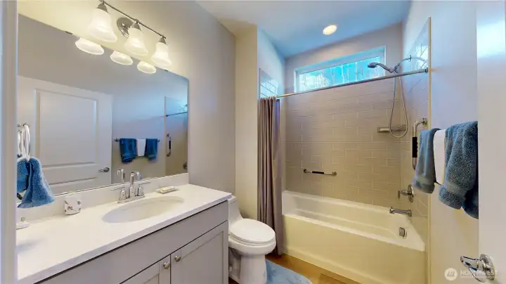Hall bath with quartz counter vanity, tile shower, and deep soaking tub.