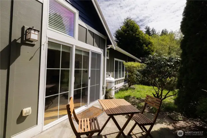 Sunny back yard garden space and patio fenced with a gate leading to the beautiful green shared open space and surrounding forest beyond.