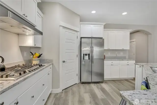 All white cabinetry, stainless steel appliances, a pantry, and a large center island add to the appeal of this kitchen.