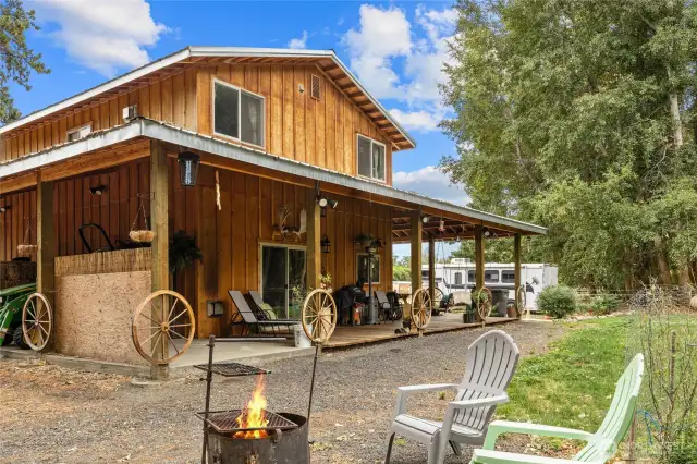Rear of the home! The covered porch feels so rustic & cozy with the wagon wheels! Lots of room for entertaining, outdoor eating space, & a firepit area.