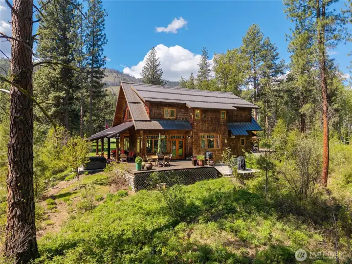 Northwest home rich in natural wood with walls of windows that invite in abundant sunlight—warm, light-filled interiors paired with expansive decks, stone patio  and covered porch for seamless indoor-outdoor living