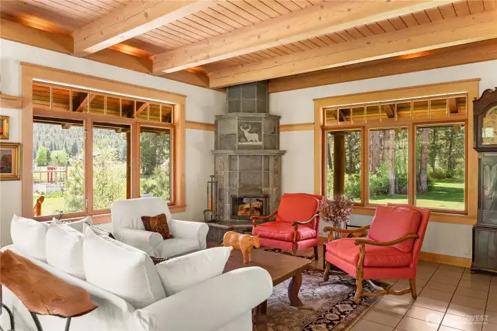 Light-filled great room with exposed timber beams and tile floors, anchored by a Tulikivi wood-fired fireplace—creating a warm, inviting gathering space