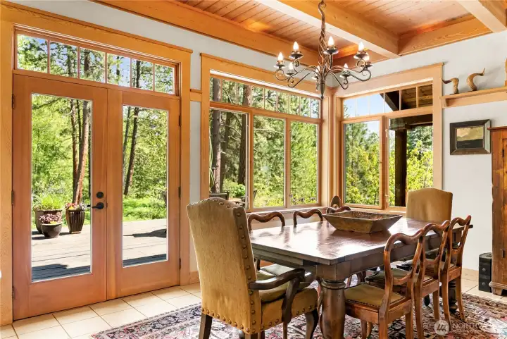 Dining area surrounded by walls of windows and French doors, filled with natural light and opening directly to the deck for effortless indoor-outdoor entertaining