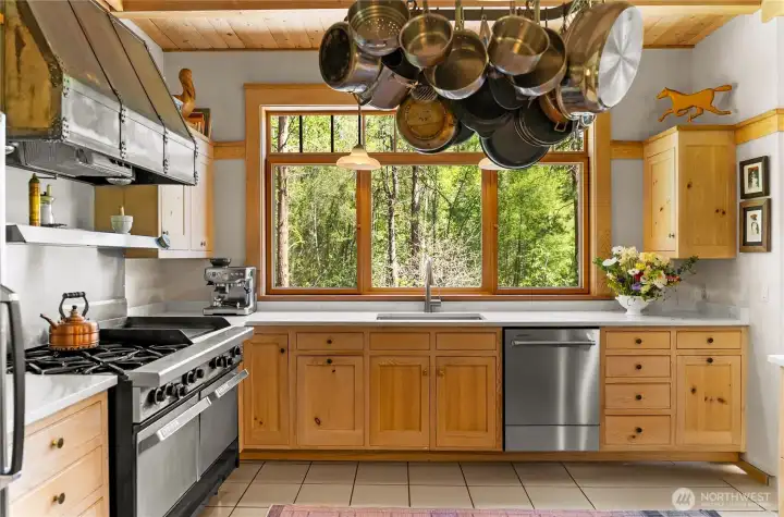 Chef’s kitchen featuring granite countertops, custom wood cabinetry, and a professional-grade Garland range, complemented by a classic hanging pot rack and expansive windows views