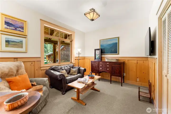 Main floor third bedroom currently used as a cozy den/TV room, featuring warm wood accents, a closet, and a large window that brings in natural light—comfortable, carpeted space ideal for guests or flexible living