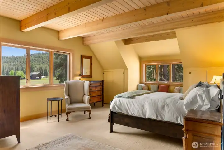 Upstairs primary ensuite retreat with vaulted ceilings, warm wood accents, and abundant natural light—featuring a charming window seat with built-in storage for added comfort and functionality
