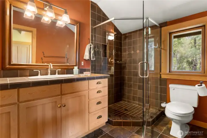 Primary bathroom with slate-tiled glass shower, slate flooring, and matching counters—warm wood cabinetry and natural light create a refined, cohesive, and timeless space