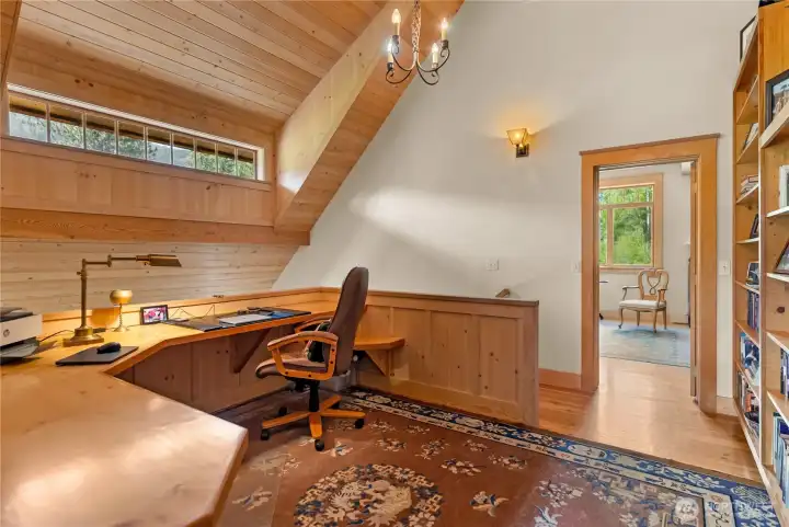 Open landing at the top of the stairs designed as a two-person home office or library, featuring a full wall of built-in bookshelving, warm wood accents, and a light-filled setting between the two ensuite bedrooms
