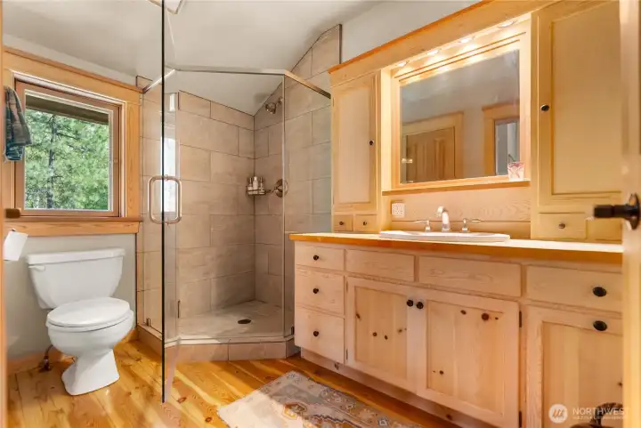 Ensuite bathroom with warm wood cabinetry, spacious vanity, and natural light—featuring a tiled shower and cohesive finishes for a comfortable, well-appointed private bath, complete with large linen closet
