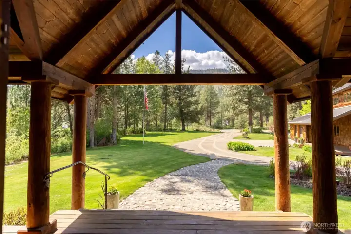 Covered front porch framed by timber beams, offering a welcoming arrival and peaceful outlook over landscaped grounds with automatic in-ground irrigation and a well-maintained graveled drive