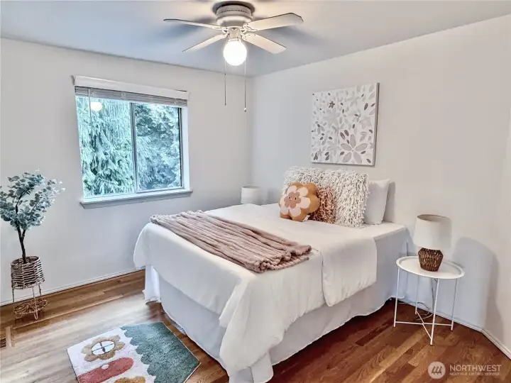 Comfortable secondary bedroom with hardwood flooring, a ceiling fan, and treed view. Perfect for family or guests.