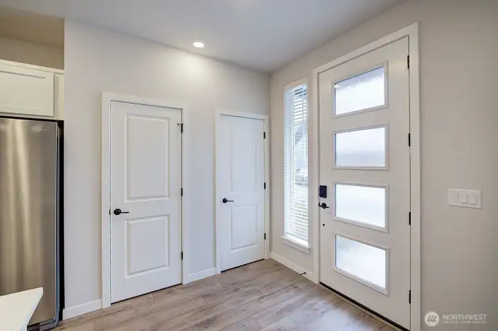 Sunlight streams in through the window panels of the front door in the entry with coat closet storage.