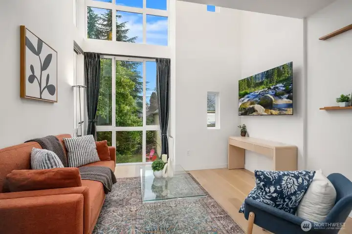 Bright and inviting living area with dramatic double-height windows, engineered hardwood floors, and a seamless connection to the outdoors through a private balcony door.