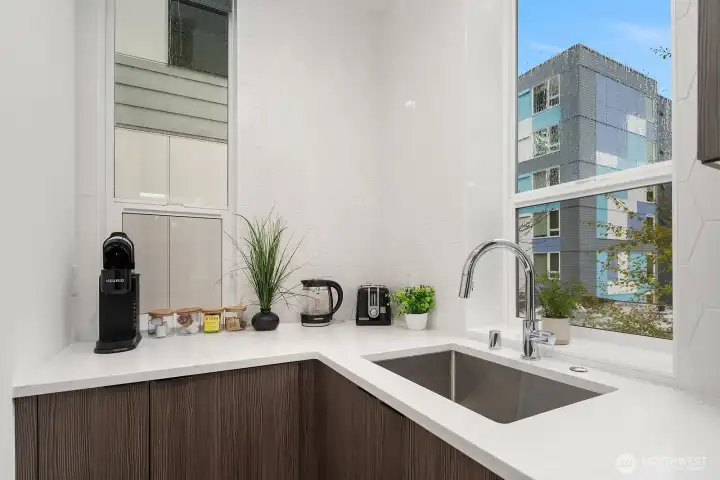 Bright kitchen with sleek quartz countertops, modern fixtures, and a large window framing an urban cityscape view, blending style and functionality in this contemporary Seattle home.