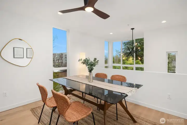 Bright and modern dining area with a sleek ceiling fan, pendant lighting, engineered hardwood floors, and a large window filling the space with natural light and neighborhood views.