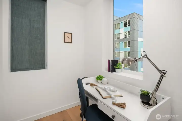 Compact and efficient home office nook with a bright window, clean white walls, and a quiet, focused atmosphere ideal for remote work in the heart of the city.