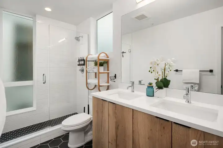 Spa-inspired primary bath with warm wood vanity, dual sinks, clean white tile, and a sleek glass shower offering a refined and tranquil retreat in this modern Seattle home.