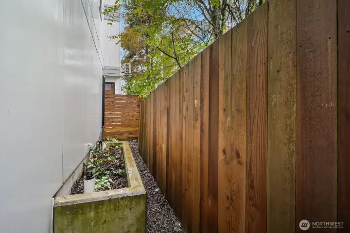 A private turf yard and cedar-fenced side garden offer a rare outdoor retreat in the heart of the city. The raised planting bed and clean concrete path create a low-maintenance urban oasis.