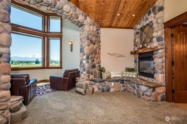 The primary bedroom suite's sitting area, with a dual-face river rock fireplace, bay windows and mountain views  .Notice how the river rock embellishes both the fireplace and the sitting area, projecting strength and enclosure.  The wood soffit ceiling provides warmth to the area as well