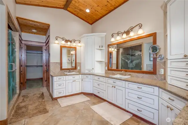 The primary bath suite has granite counters, radiant heated tile floors, extensive cabinets and drawers, a wood soffited ceiling, and walk-in shower and closet