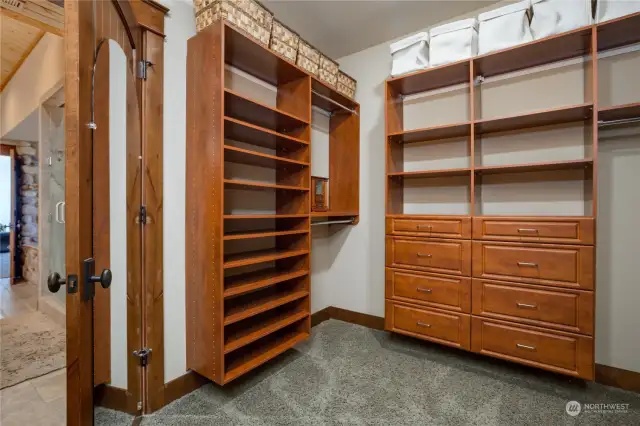 The primary suite's walk-in closet, with built-in organizer shelving, drawers, extensive hanging spaces and carpeted flooring.  There is a full-length mirror on the door