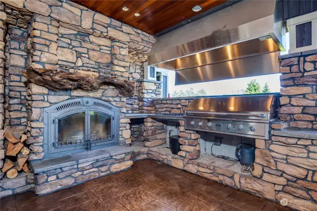 The outside covered porch fireplace and barbecue area, with professional grade appliances and rock walls.  Notice also the burl wood fireplace mantle and wood soffit ceiling, with recessed can lighting