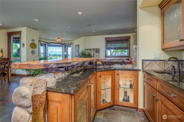 The wet bar adjacent to both the family room and kitchen areas features burl wood and granite counters, and glass-faced cabinets