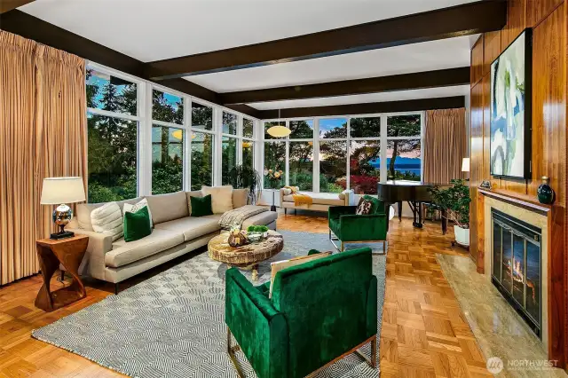 Designed by renowned architects Tucker & Shields, the Living Room embraces its south and west exposures with floor-to-ceiling windows that frame glimpses of Puget Sound, mature gardens, and glowing sunsets. Exposed beams, warm paneling, and original parquet flooring evoke mid-century sophistication—while the room’s generous scale and enduring materials ground it firmly in Magnolia’s architectural legacy.
