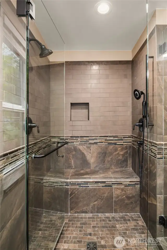 Large walk-in shower with double shower heads and seat.