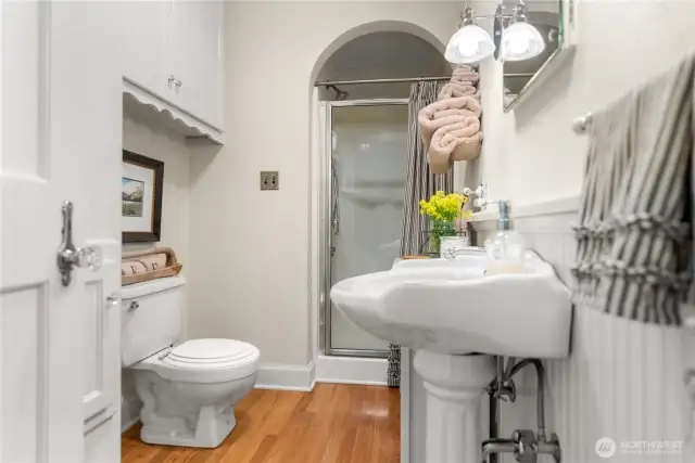 Main floor bath features classic charm with pedestal sink, walk-in shower, built-in storage, and warm hardwood floors—blending vintage detail with everyday comfort.