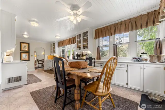 Charming farmhouse kitchen features vintage glass-front cabinets, multiple prep areas, and an inviting eat-in nook surrounded by windows and natural light.