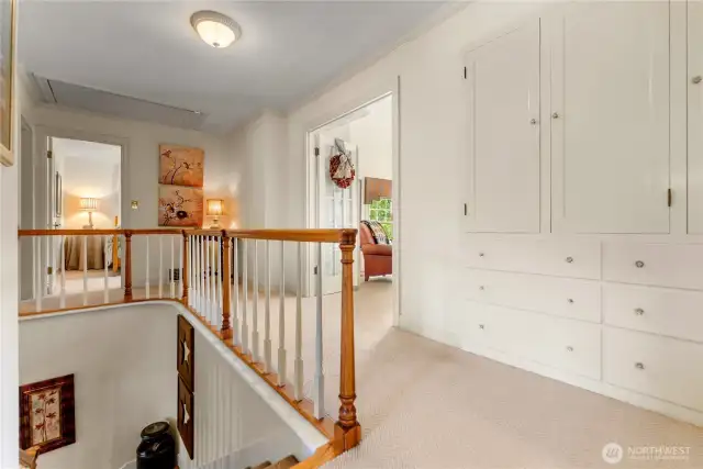 Upper landing with charming built-in cabinetry and elegant wood railings that add a graceful touch to the stairwell—an inviting space connecting light-filled bedrooms and the top deck beyond.
