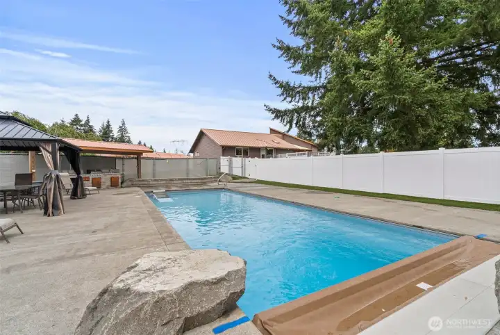 16x40 inground heated pool is surrounded by exposed aggregate and bordered by maintenance-free ForeverLawn Astroturf for a clean, soft finish. Equipped with a robot pool cleaner and skimmer, it offers effortless upkeep, while a  pool cover ensures year-round care. Fully fenced for complete privacy.