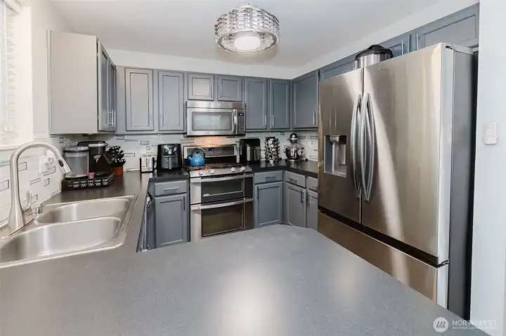 Kitchen with modern backsplash, stainless steel appliances, and updated lighting.