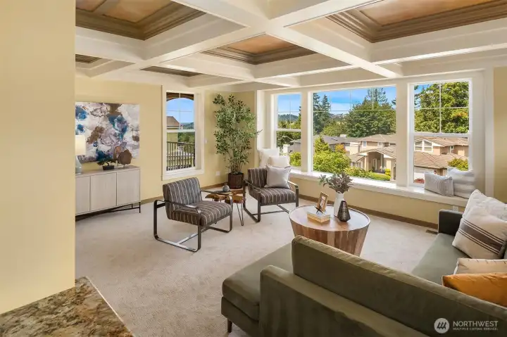 The light-filled family room is framed by oversized windows, a distinctive coffered ceiling, and peek-a-boo views—an inviting place to relax just beyond the kitchen. The light-filled family room is framed by oversized windows, a distinctive coffered ceiling, and peek-a-boo views—an inviting place to relax just beyond the kitchen.