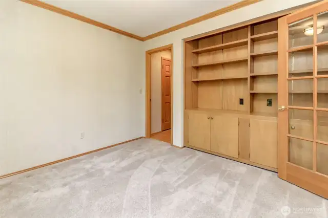 Den/office has ample cabinets and bookshelves. You can see door leading out to the garage in the background.