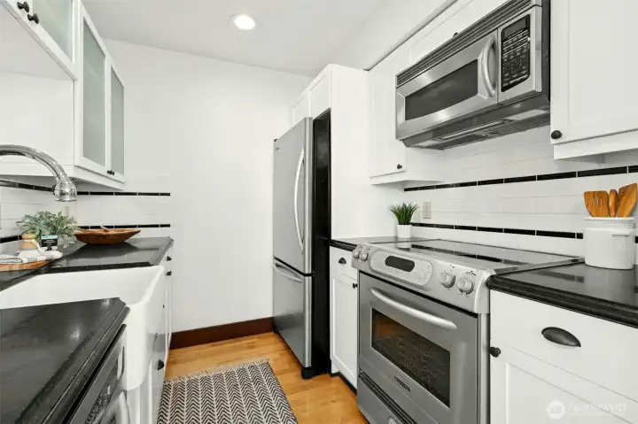 The efficient kitchen offers a farm-style sink, subway tile backsplash, glass-front cabinets, & stainless-steel appliances