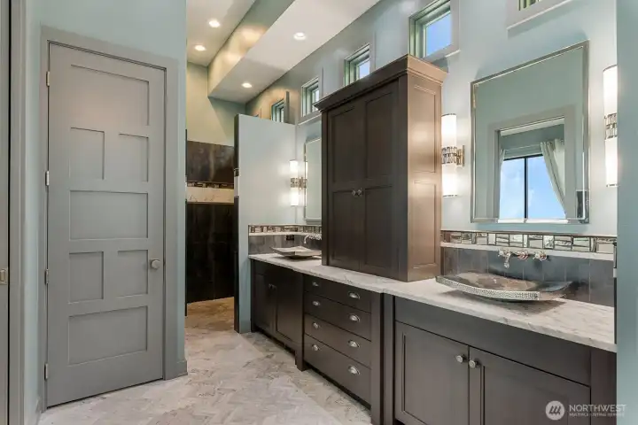 The primary spa bath offers heated marble floors, dual vanities with custom cabinetry, a limestone soaking tub, walk-in shower, separate water closet, and a spacious walk-in closet — designed for comfort, privacy, and everyday indulgence.