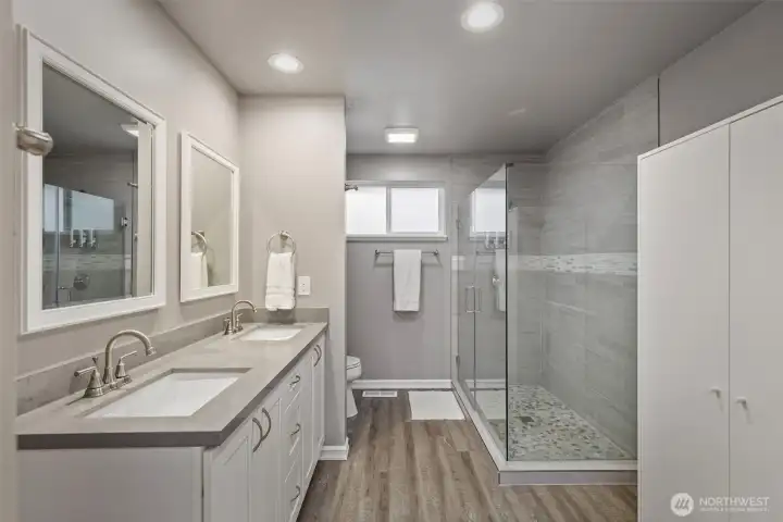 Stylishly updated 3/4 bath features a large custom tiled shower, double vanities, and armoire closet on the right.
