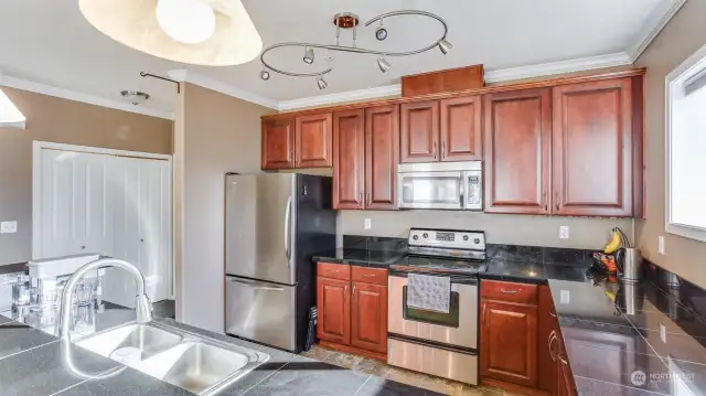 Open kitchen boasts natural cabinetry, beautiful countertops, and stainless steel appliances.