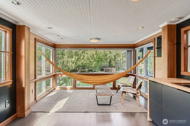 This stunning sunroom is the ultimate lakefront escape—framed by expansive windows and crowned with a fully opening Euro-style glass wall, it blurs the line between indoors and out. Lounge in the hammock (yes, it stays!) and let the peaceful water views, gentle breezes, and rustling trees wash over you. Whether you're enjoying morning coffee, a good book, or an afternoon nap, this space embodies the tranquil essence of floating home living. Thoughtful details like wood trim, natural light, and serene water views make it a one-of-a-kind retreat.