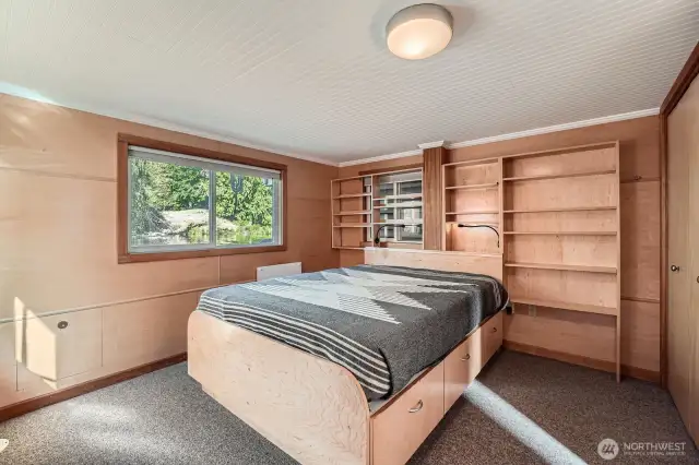 The primary bedroom is located off the open water channel, with built in bes, drawers below and a wall of book/decor shelving. Add baskets for additional storage. The closet is to the right.